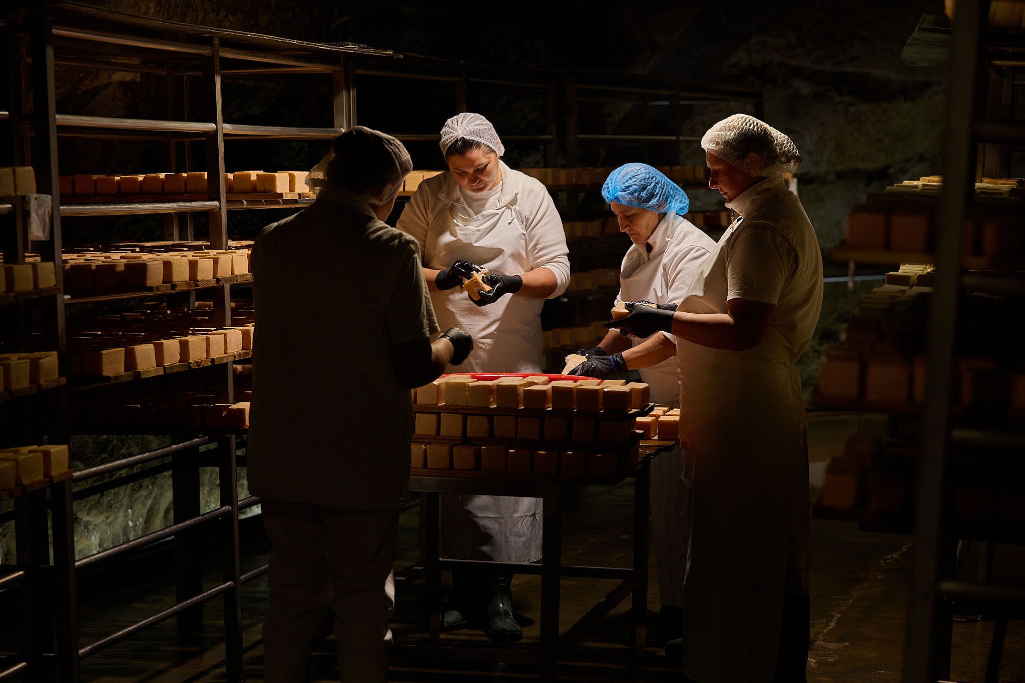 four women around a stack of cheese washing their rinds in Țaga Cave